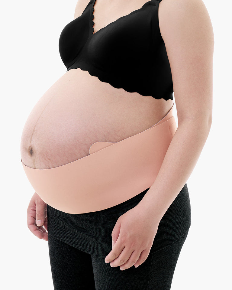 Translation missing: en.Light beige Momcozy Maternova belly band shown on a pregnant model wearing a black bra and grey leggings
